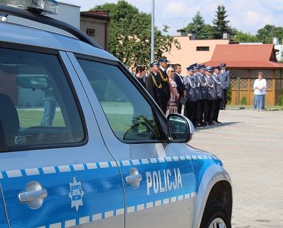 Zdjęcie przedstawia radiowóz policyjny. Na drugim planie fotografii widać uczestników obchodów Święta Policji.