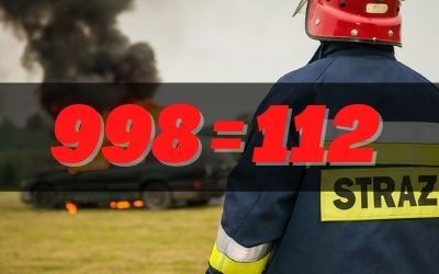 Numer 998 równa się 112, a w tle strażak i płonący samochód. Strażak ubrany w kurtkę z napisem "strażak".