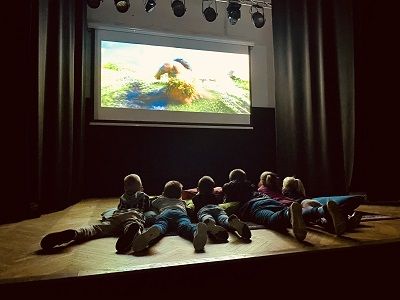 Dzieci leżące na dywanie oglądające projekcje filmu.